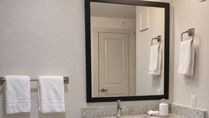 Un baño con inodoro, lavamanos, espejo y perchero para toallas.