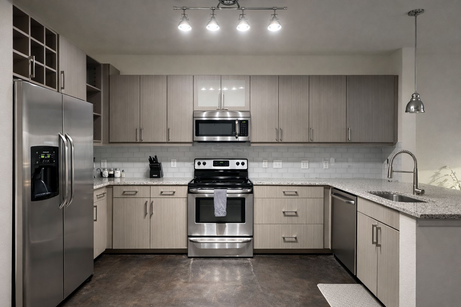 A modern kitchen with stainless steel appliances, light wood cabinets, and a granite countertop.