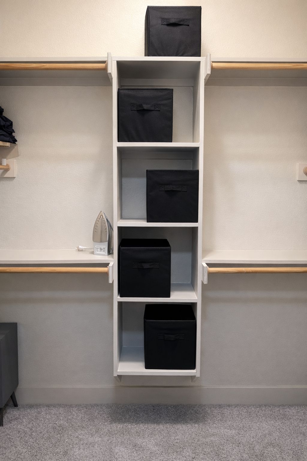 Une étagère blanche avec des boîtes de rangement noires, placée contre un mur de couleur claire.