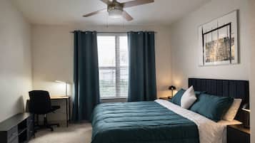A bedroom with a bed, desk, chair, and a ceiling fan.