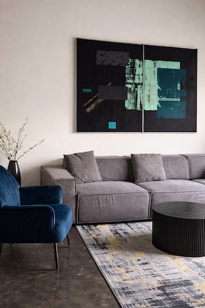 A modern living room with a grey sofa, a blue armchair, and a black coffee table. - DT Corporate Condo NR Farmers Market w/ Gym Pool (Dallas)