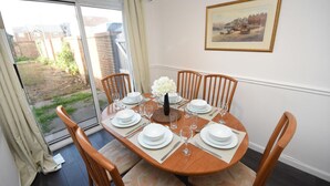 A dining area with a table set for four, chairs, a vase with flowers, and a framed picture on the wall. - Beautiful 3BRHome with a large garden in Colchester (Colchester)