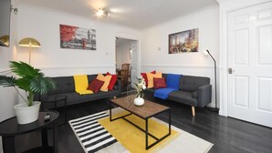 A modern living room with two sofas, a coffee table, a potted plant, and artwork on the walls. - Beautiful 3BRHome with a large garden in Colchester (Colchester)