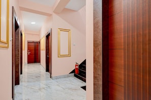 Un pasillo con suelo de mármol, puertas de madera con marcos dorados y un extintor en la pared.