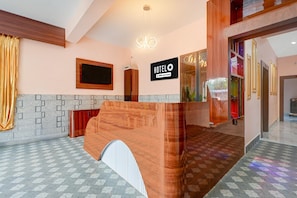 Zona de recepción de un hotel con un mostrador de madera, un reloj digital y un cartel que indica que el hotel es administrado por OYO.