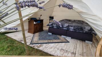 Una tienda de campaña con una cama, un pequeño armario de madera y una alfombra.