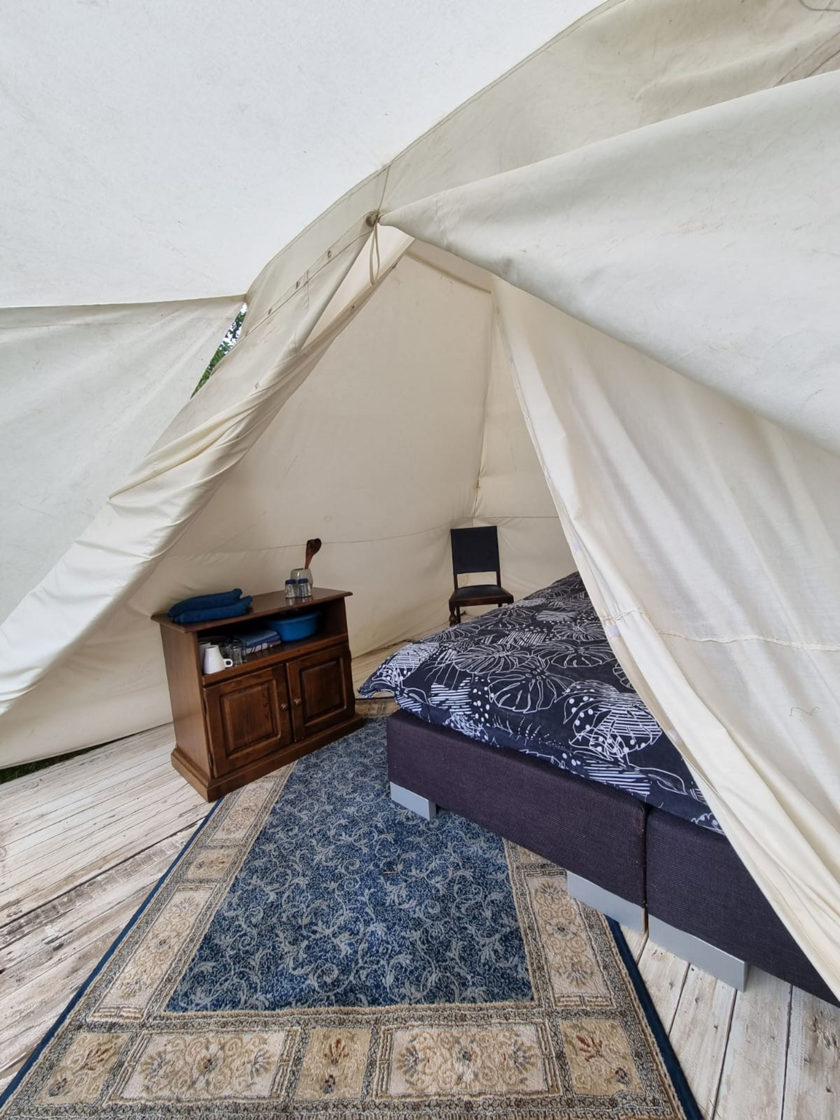 Una tienda de campaña con una cama, un pequeño armario de madera y una silla.