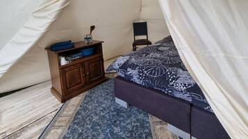 Una tienda de campaña con una cama, un pequeño armario de madera y una silla.