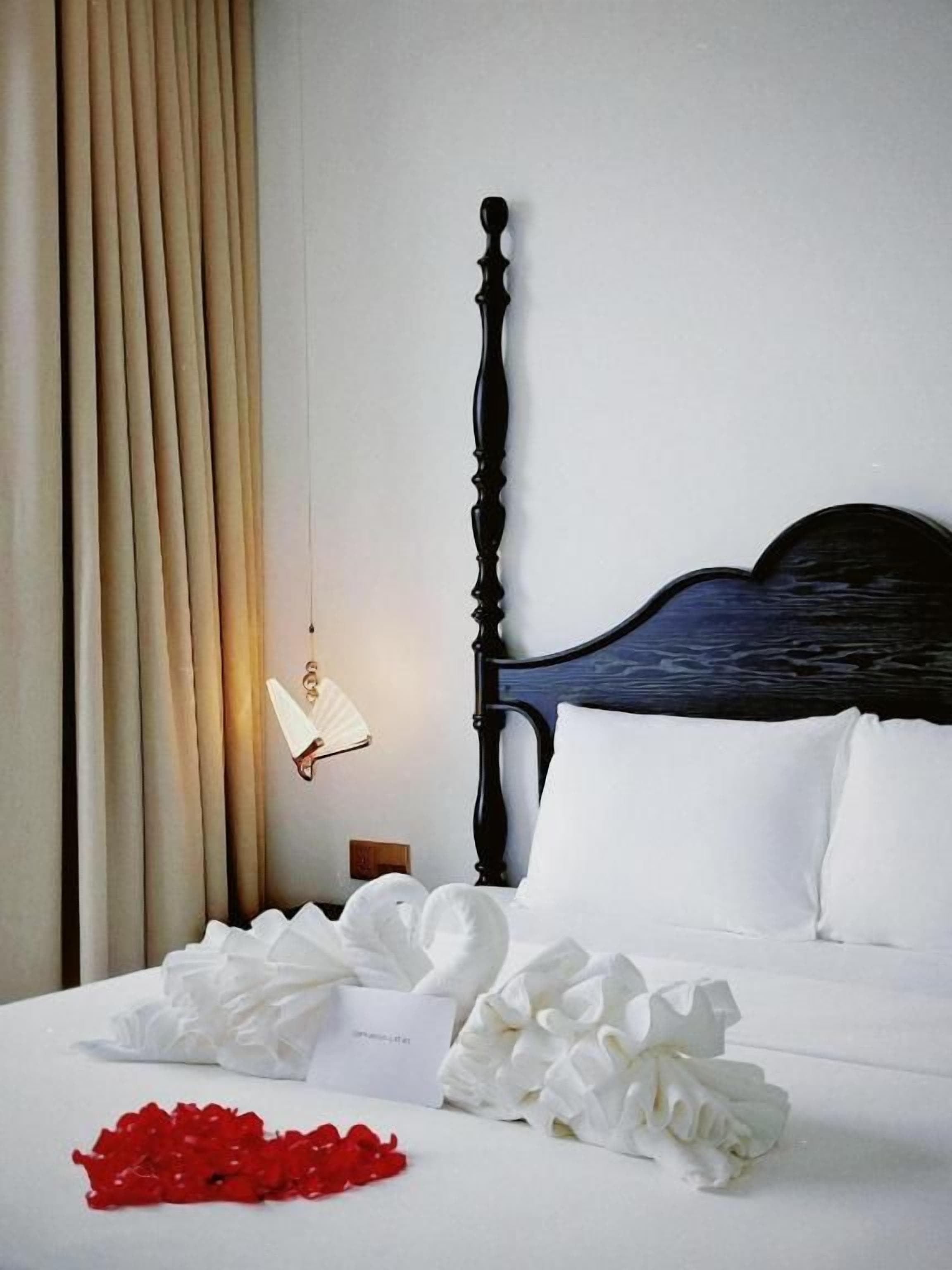 A hotel room with a bed, a nightstand, a wall-mounted fan, and a curtain.