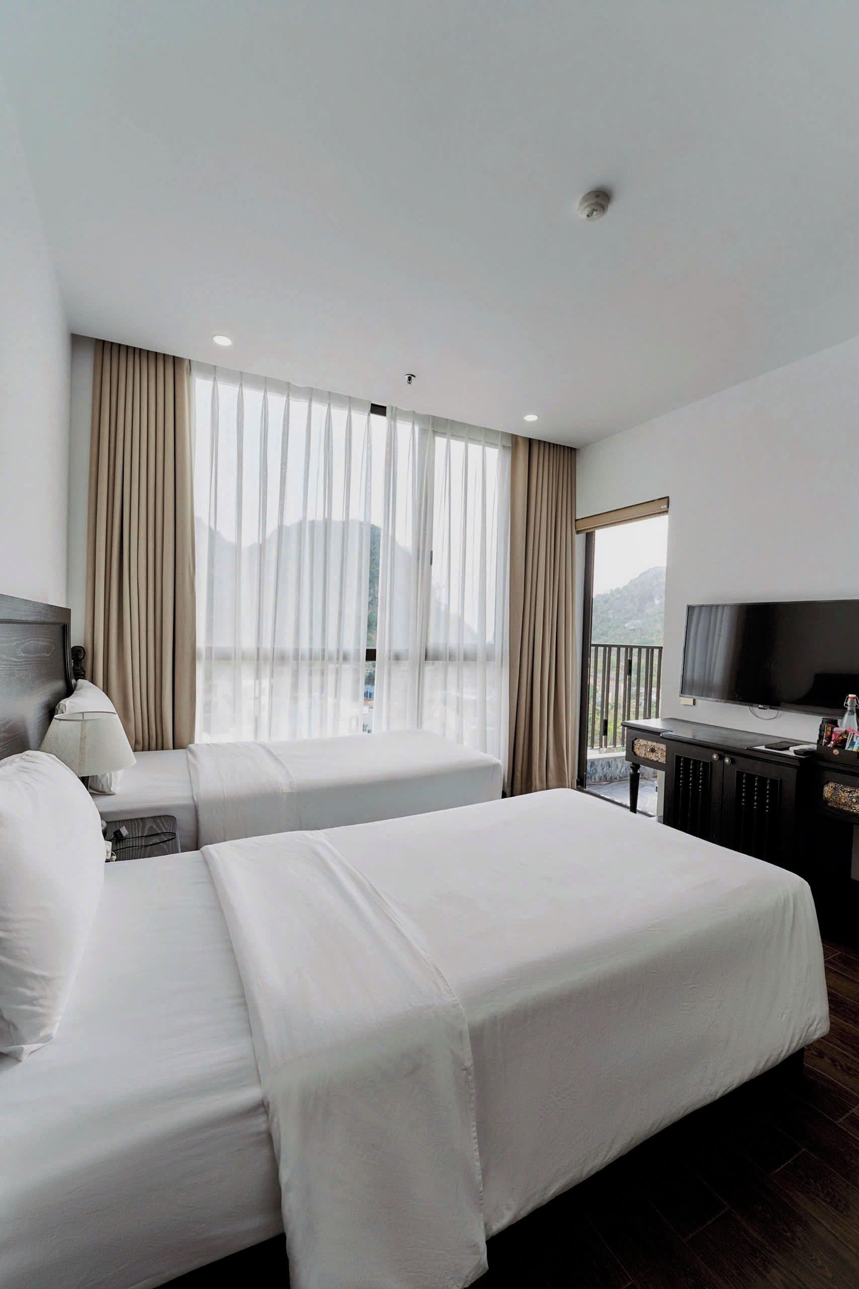 A hotel room with two beds, a TV, and a balcony with a view.