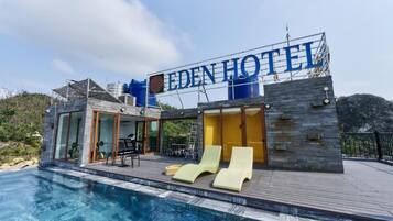 A modern hotel with a pool, lounge chairs, and a sign reading 'EDEN HOTEL'.