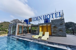 Un hotel moderno con piscina, sillones de descanso y un cartel que dice 'EDEN HOTEL'.