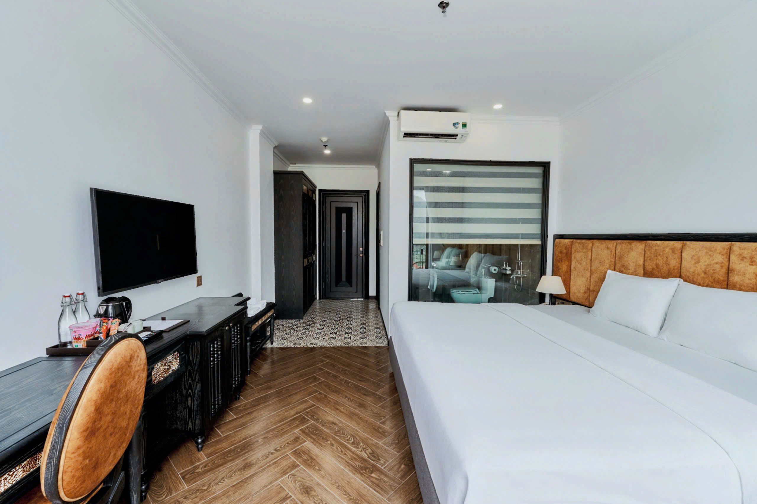A hotel room with a bed, desk, chair, television, and an air conditioning unit.