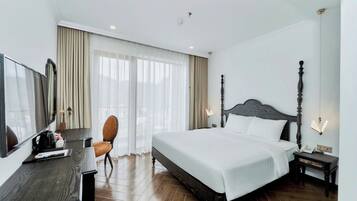 A hotel room with a bed, a desk, a chair, a bedside table, and a mirror.