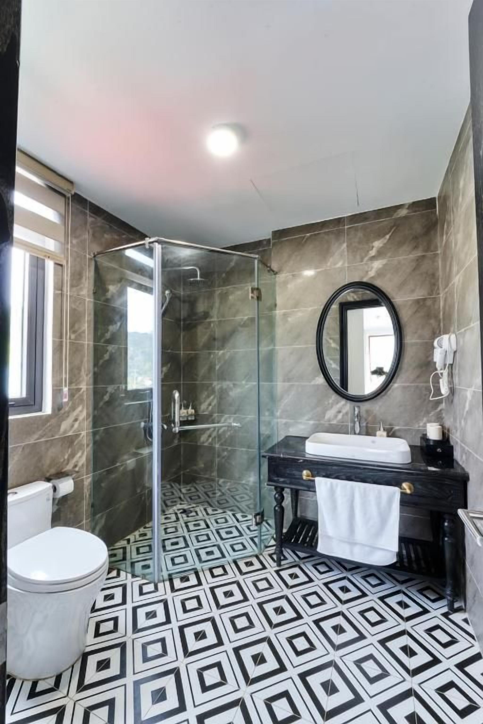 A bathroom with a glass shower enclosure, a toilet, a sink with a mirror, and patterned floor tiles.