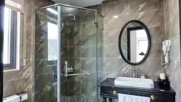 A bathroom with a glass shower enclosure, a toilet, a sink with a mirror, and patterned floor tiles.