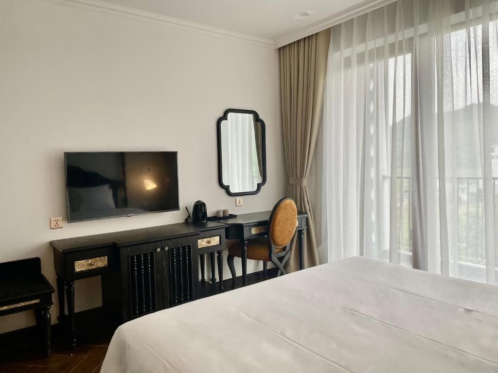 A hotel room with a bed, a desk with a chair, a television, and a window with curtains.