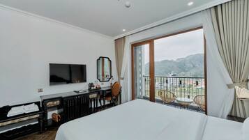 A hotel room with a bed, a desk with a chair, a television, and a balcony with a view of the mountains.