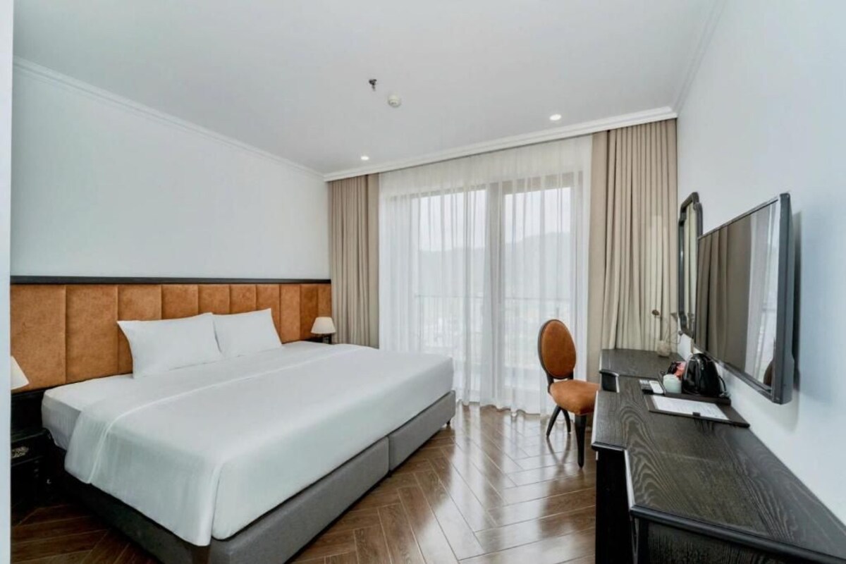 Een hotelkamer met een bed, een bureau, een stoel, een televisie en een raam met gordijnen.