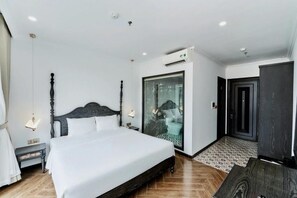 Een moderne hotelkamer met een groot bed, een douchecabine van glas en een vloer van donker hout.