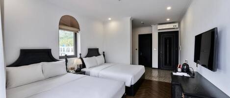 A hotel room with two beds, a TV, a desk, and an arched window.