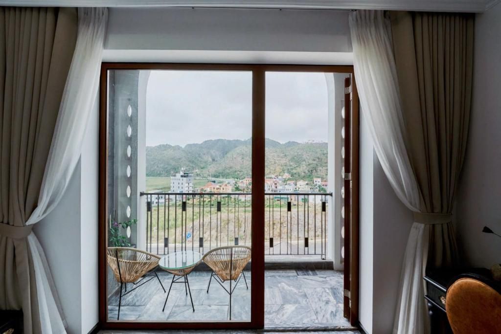 A room with a sliding glass door leading to a balcony with two wicker chairs and a table.