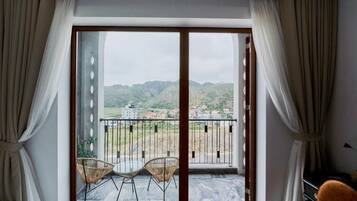 A room with a sliding glass door leading to a balcony with two wicker chairs and a table.