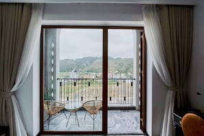 Una habitación con puerta corrediza de vidrio que da a un balcón con dos sillas de mimbre y una mesa.