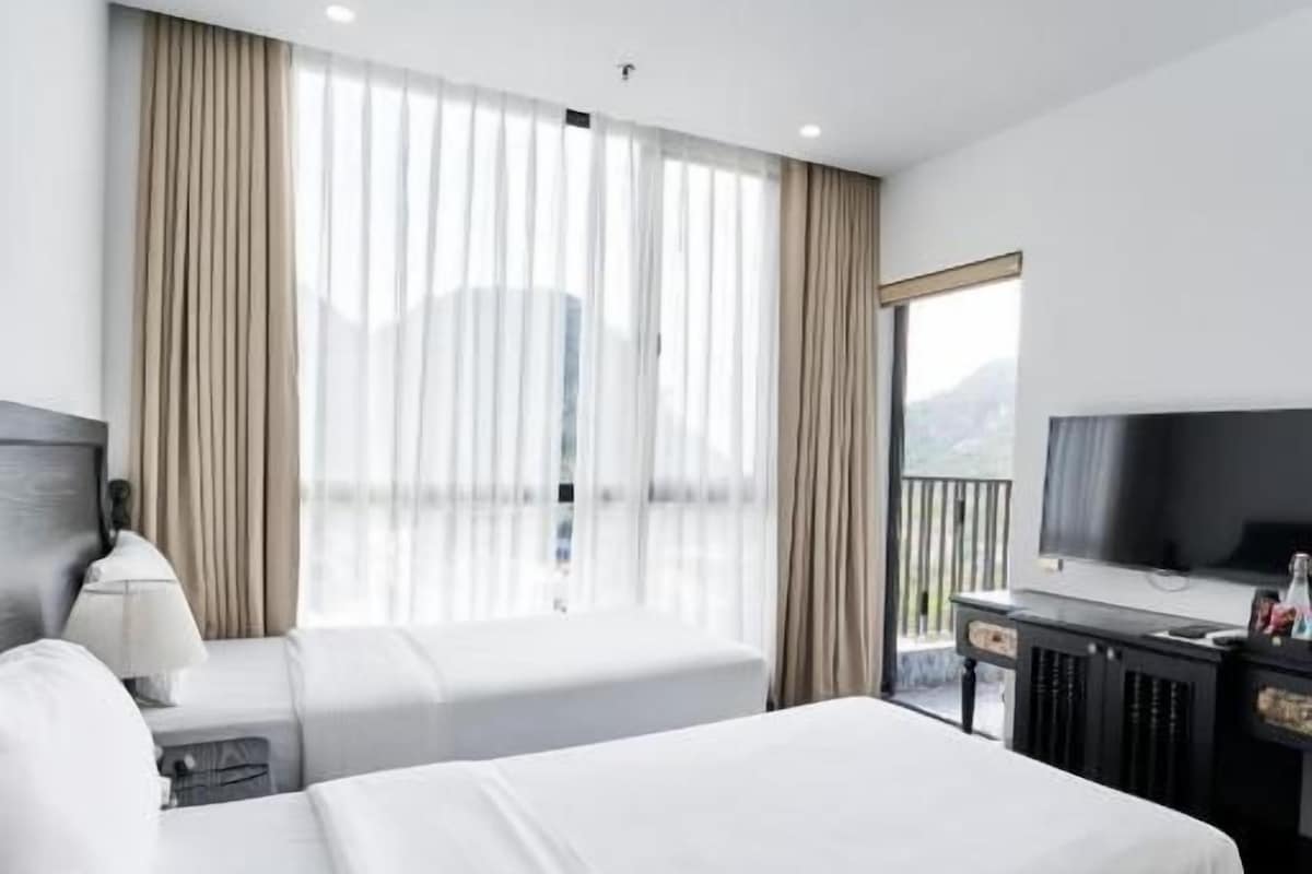 A hotel room with two beds, a TV, a desk, and a window with curtains.