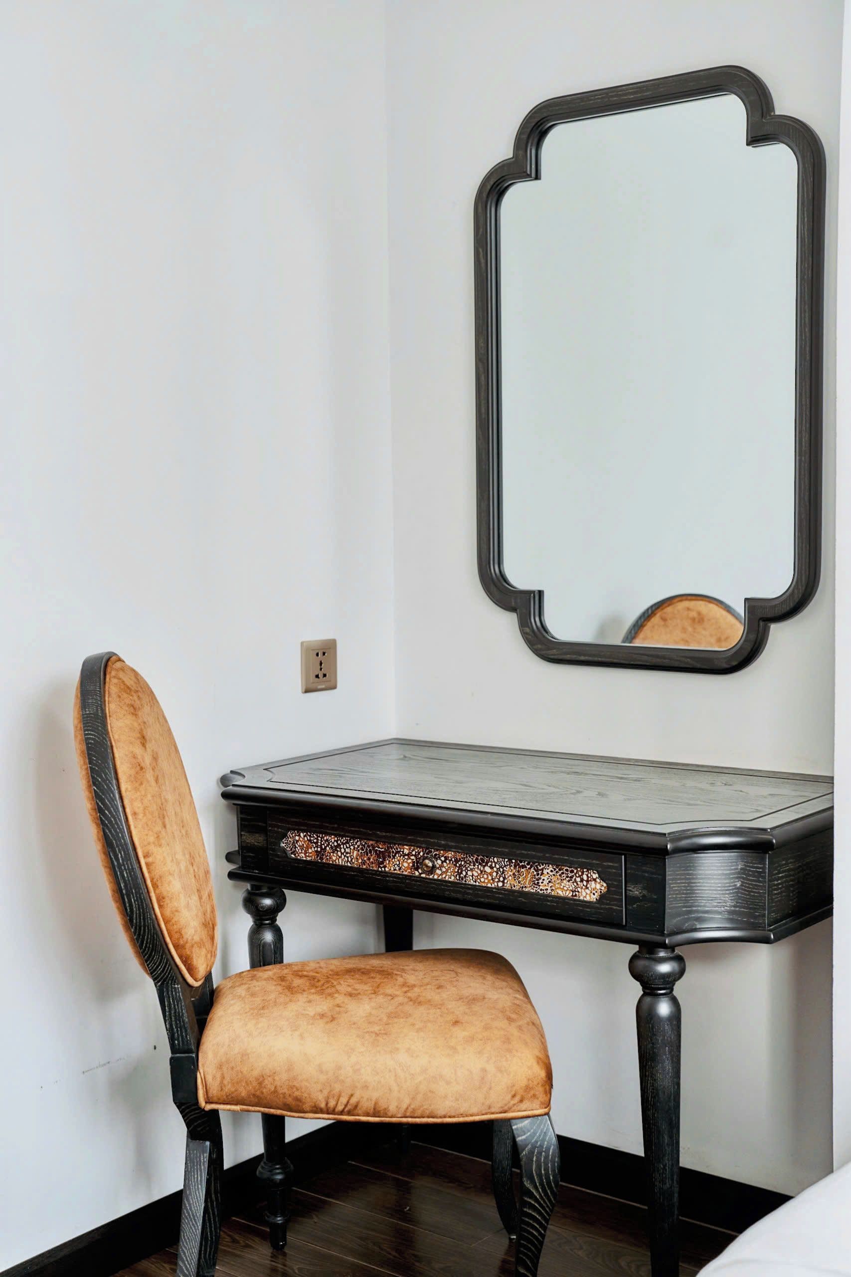 A room with a dark wooden desk, a chair with a cushioned seat, and a mirror with a black frame.