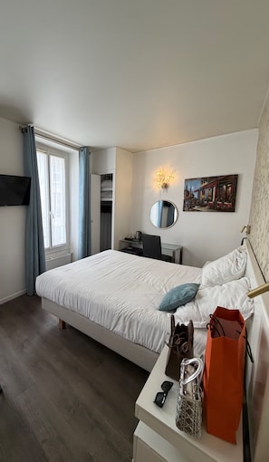 A hotel room with a bed, desk, chair, and a painting on the wall. - Vrbo Property (Paris)
