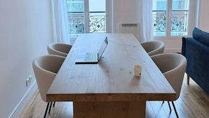 Ein Zimmer mit einem Holztisch, vier Stühlen, einem Laptop und einer Tasse auf dem Tisch.