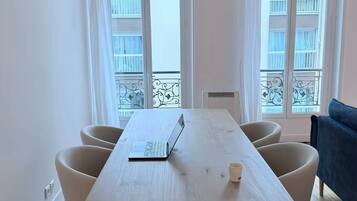 Una habitación con una mesa de madera, cuatro sillas, una computadora portátil y una taza sobre la mesa.