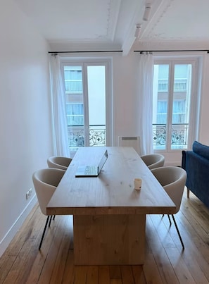 A room with a wooden dining table, four chairs, a laptop, and a cup on the table. - Vrbo Property (Paris)