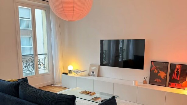 Ein modernes Wohnzimmer mit einer Couch, einem Glastisch, einem Fernseher und einer dekorativen Papierlaterne.