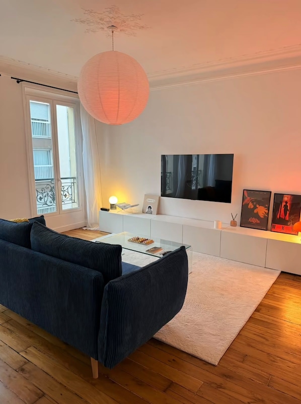 A modern living room with a sofa, a glass coffee table, a TV, and a decorative paper lantern. - Vrbo Property (Paris)