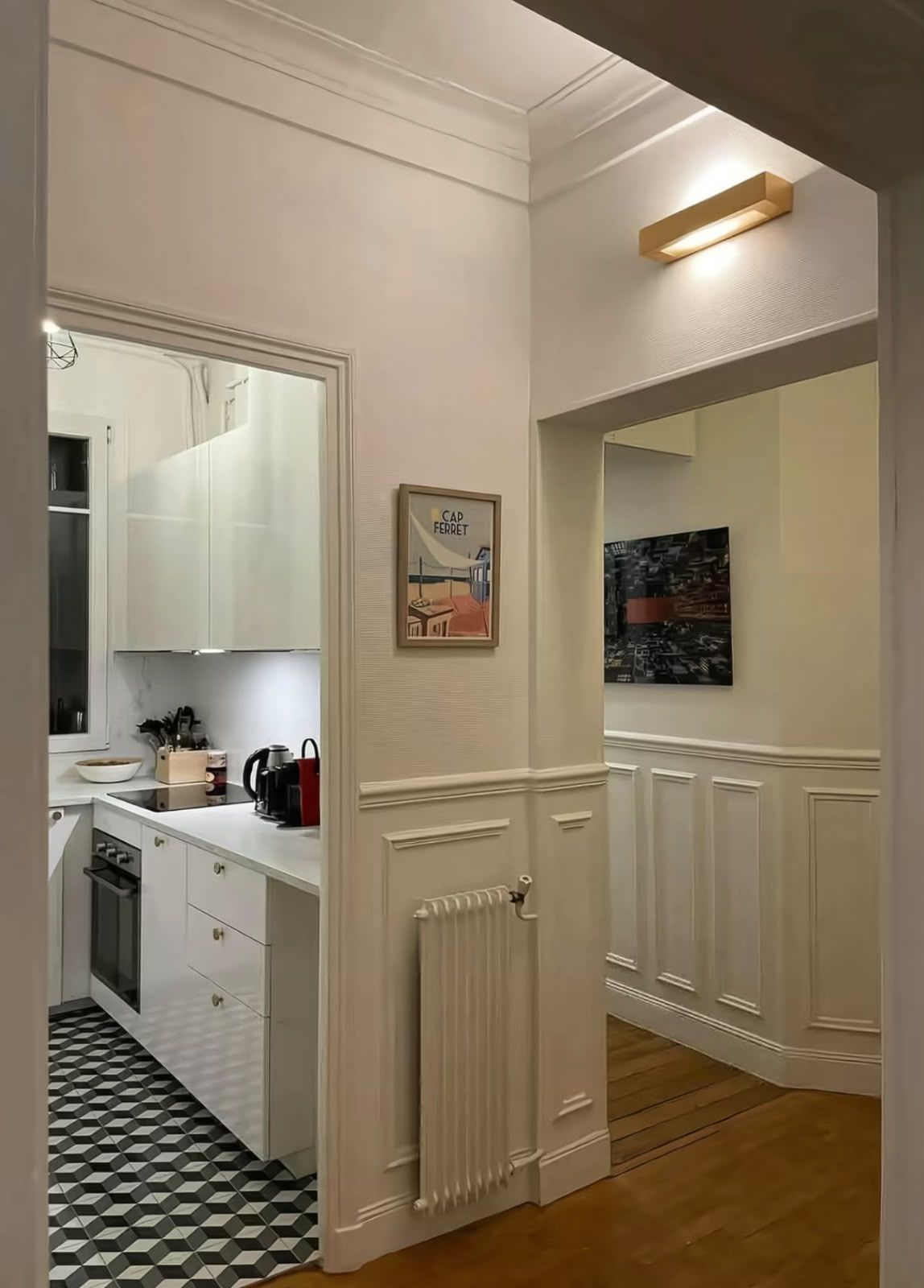 Una cocina moderna con armarios blancos, piso de baldosas blanco y negro y un radiador.