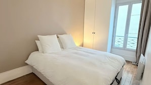 Ein Schlafzimmer mit einem Bett, Holzboden, einem Kleiderschrank und einem Fenster mit Vorhängen.