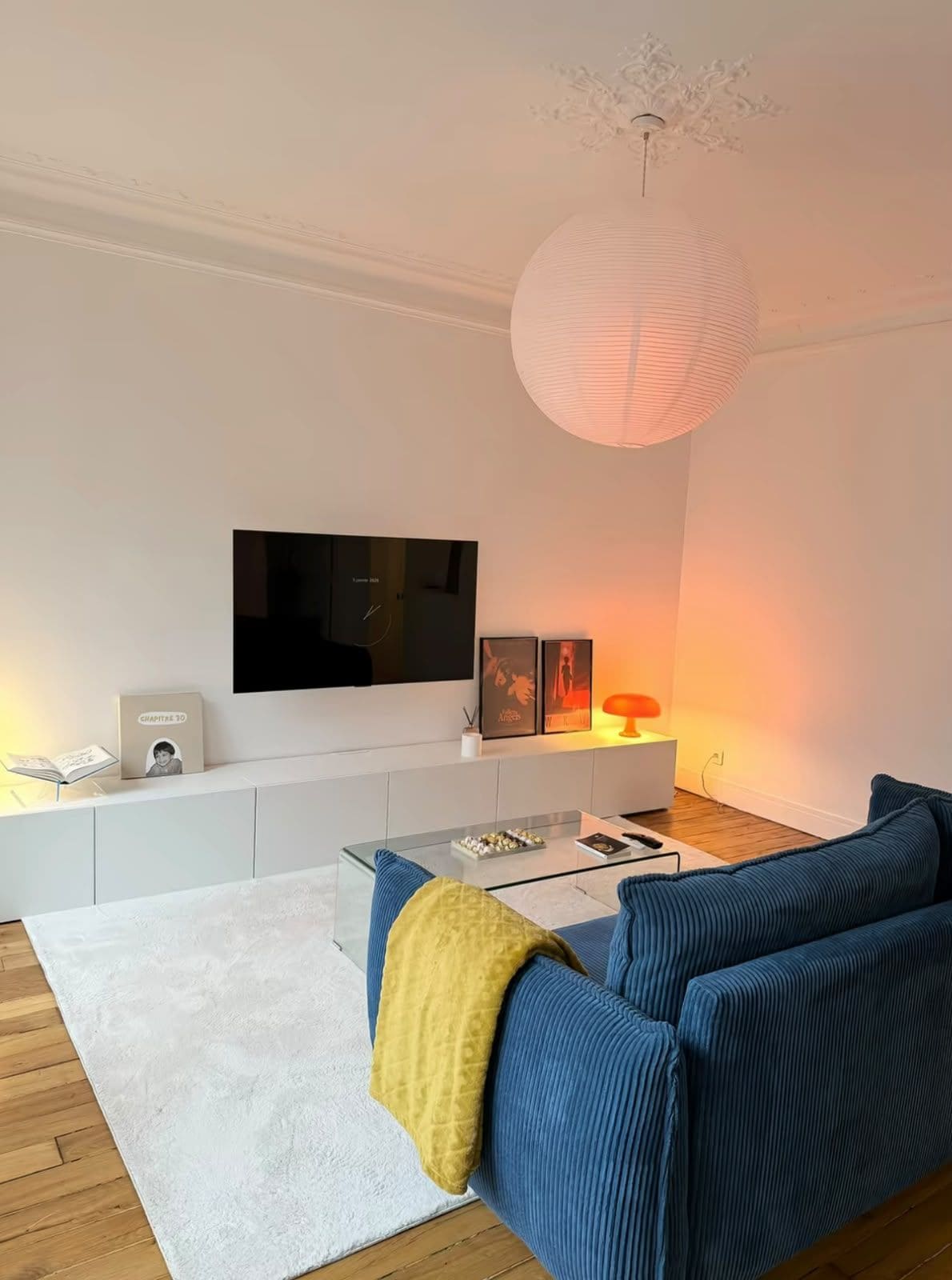 Una sala de estar moderna con un televisor de pantalla plana, un sofá, una mesa de centro e iluminación colgante.