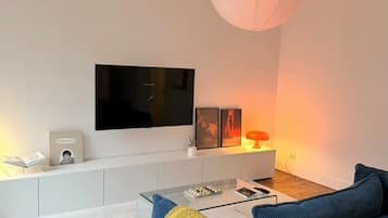 Una sala de estar moderna con un televisor de pantalla plana, un sofá, una mesa de centro e iluminación colgante.