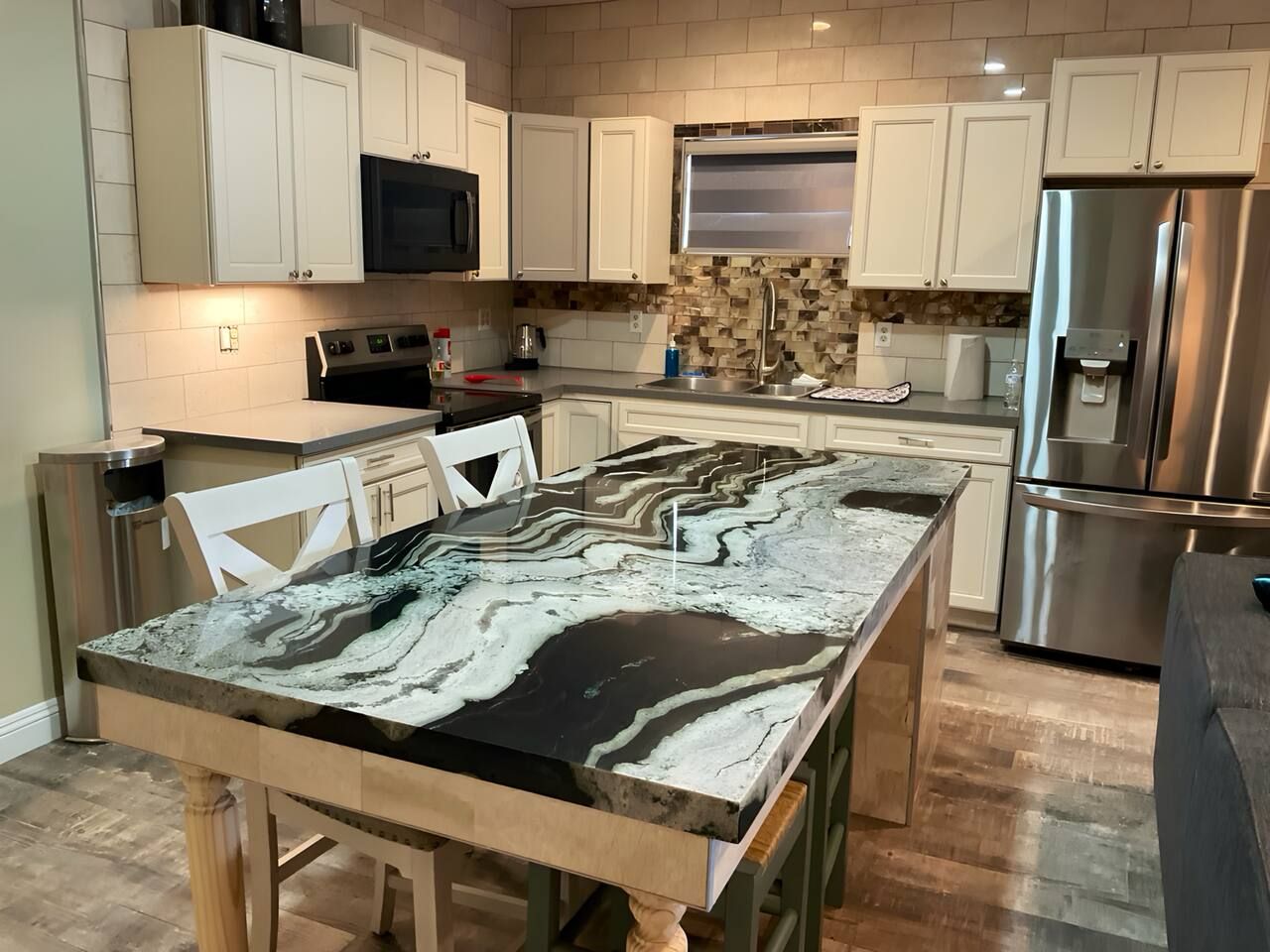 A kitchen with white cabinets, a stainless steel refrigerator, a marble countertop, and a built-in oven.