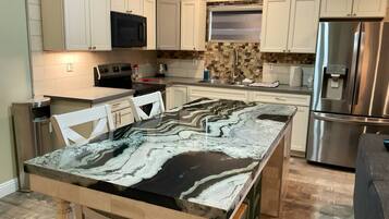A kitchen with white cabinets, a stainless steel refrigerator, a marble countertop, and a built-in oven.