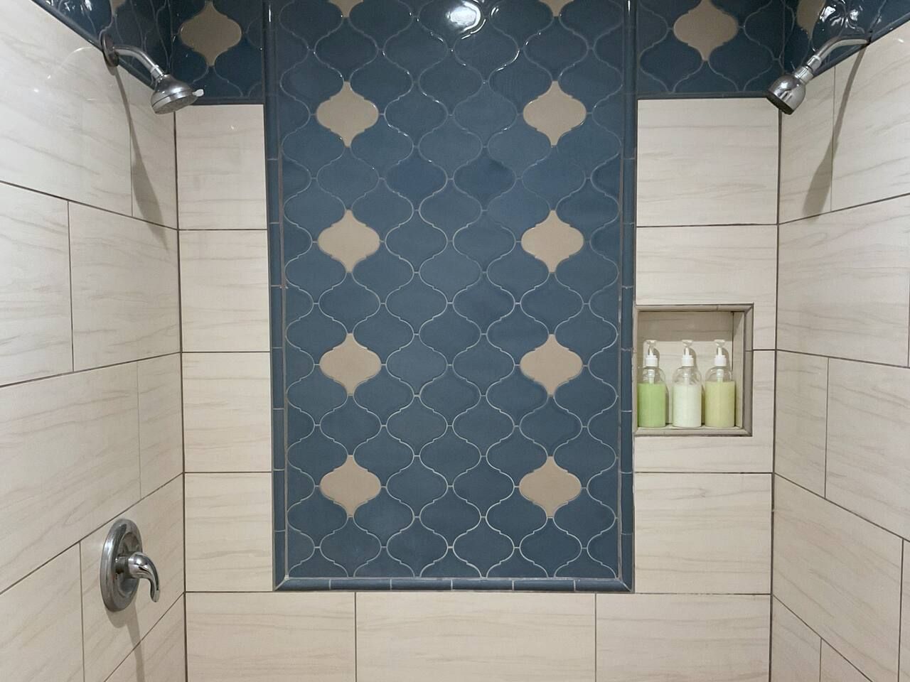 A shower area with a patterned wall, a shelf with toiletries, and a showerhead.