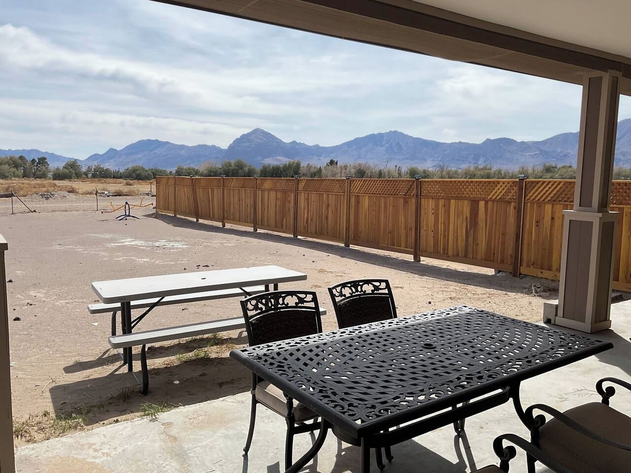 An outdoor patio with picnic tables and chairs, a wooden fence, and mountains in the background.
