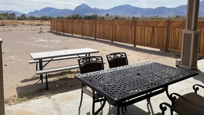 An outdoor patio with picnic tables and chairs, a wooden fence, and mountains in the background. - Updated near Death Valley, large outdoor space (Amargosa Valley)