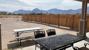 An outdoor patio with picnic tables and chairs, a wooden fence, and mountains in the background.