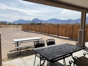 Un patio exterior con mesas y sillas de picnic, una valla de madera y montañas al fondo.