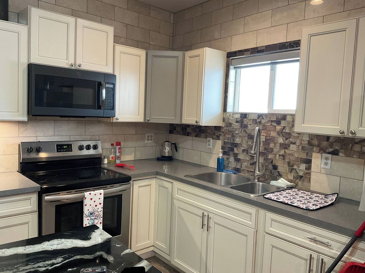 A kitchen with white cabinets, a black microwave, a stove, and a tiled backsplash.