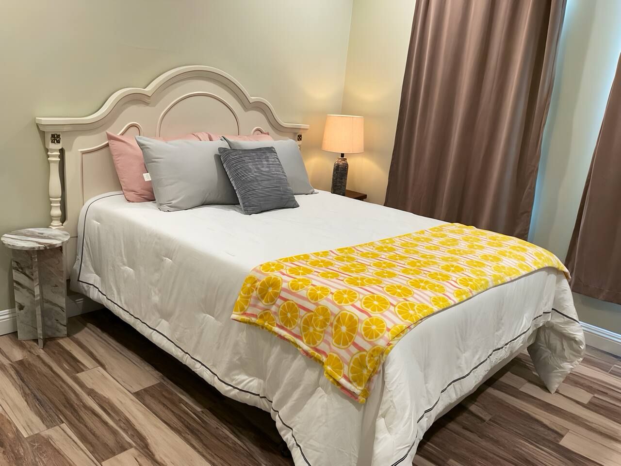 A bed with a white bedspread and a yellow-orange patterned throw blanket.
