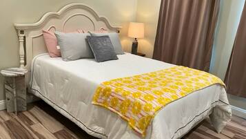 A bed with a white bedspread and a yellow-orange patterned throw blanket.
